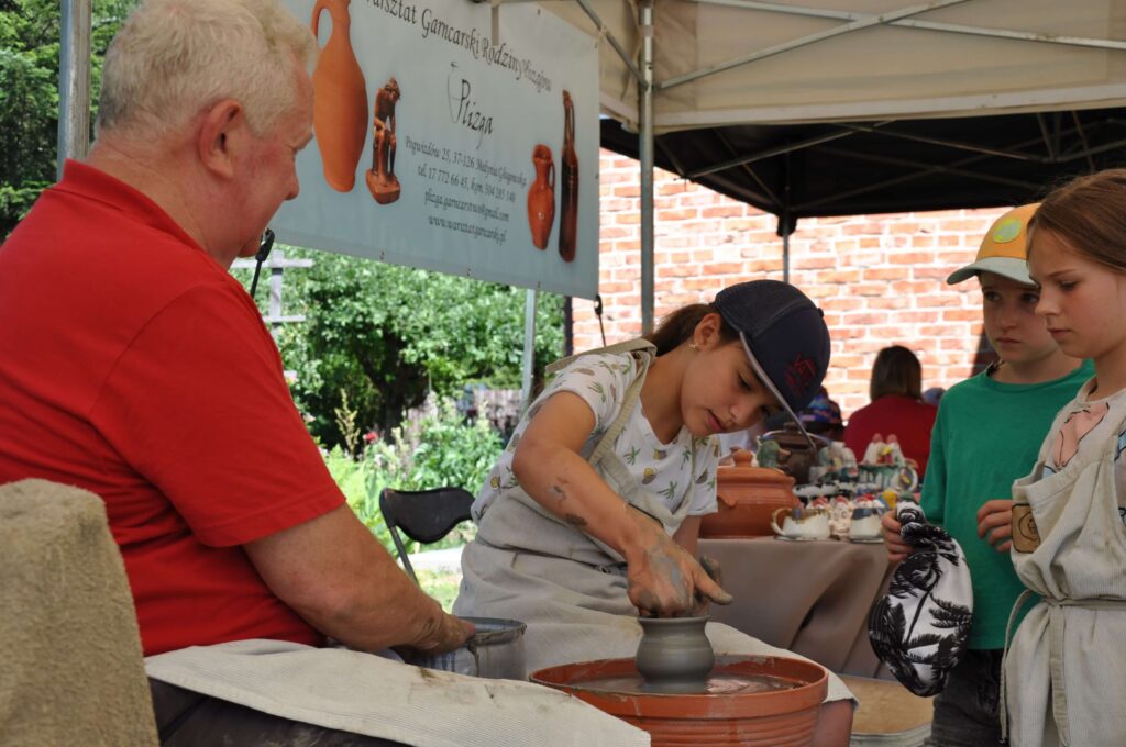 Mężczyzna i troje dzieci pracują nad ceramiką na kole garncarskim.