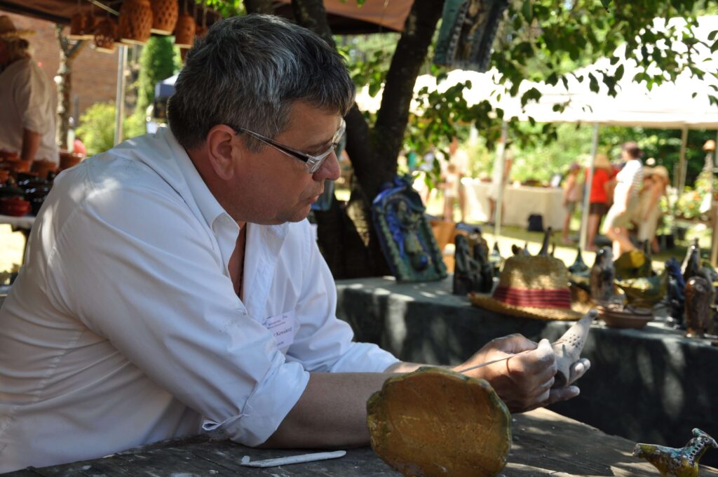 Mężczyzna ubrany w białą koszulę tworzy przedmiot z gliny.