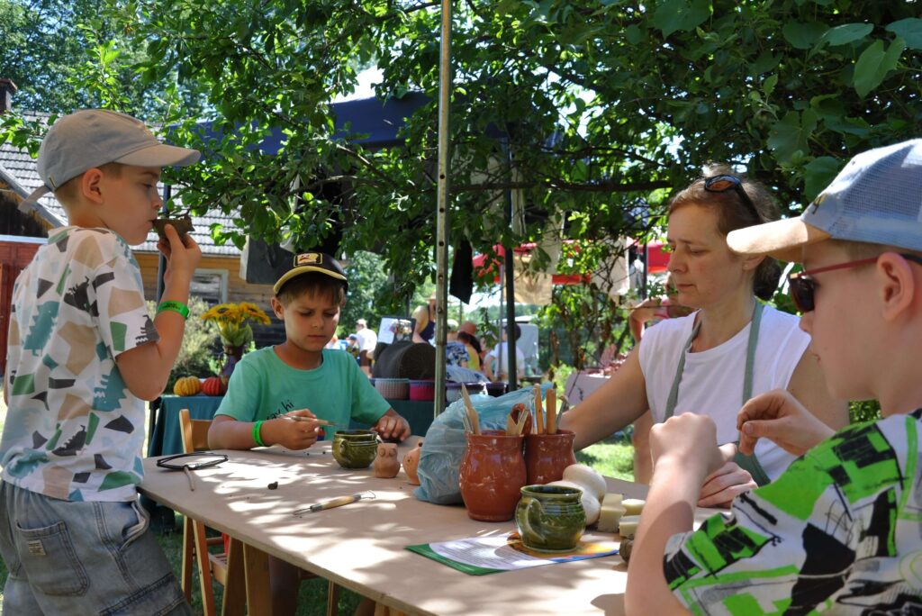 Grupa ludzi siedzi przy stole, tworząc różne przedmioty z gliny.