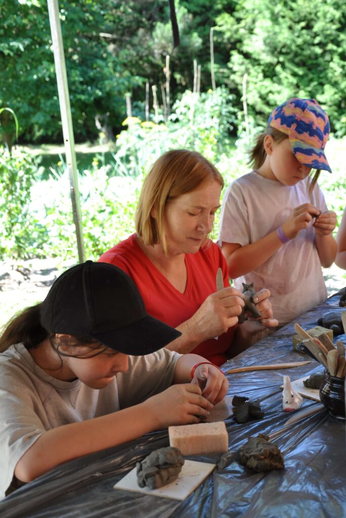 Kobieta i dwie dziewczynki wykonują ręcznie różne przedmioty z gliny.