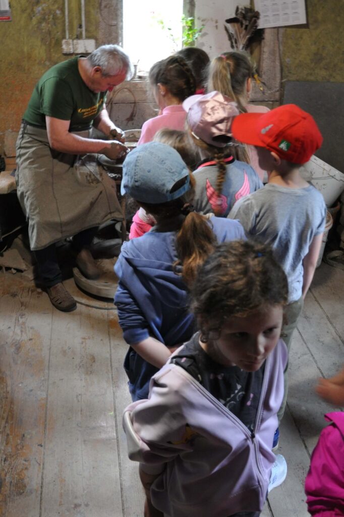 Grupa dzieci stoi wokół mężczyzny, który pracuje na kole garncarskim.