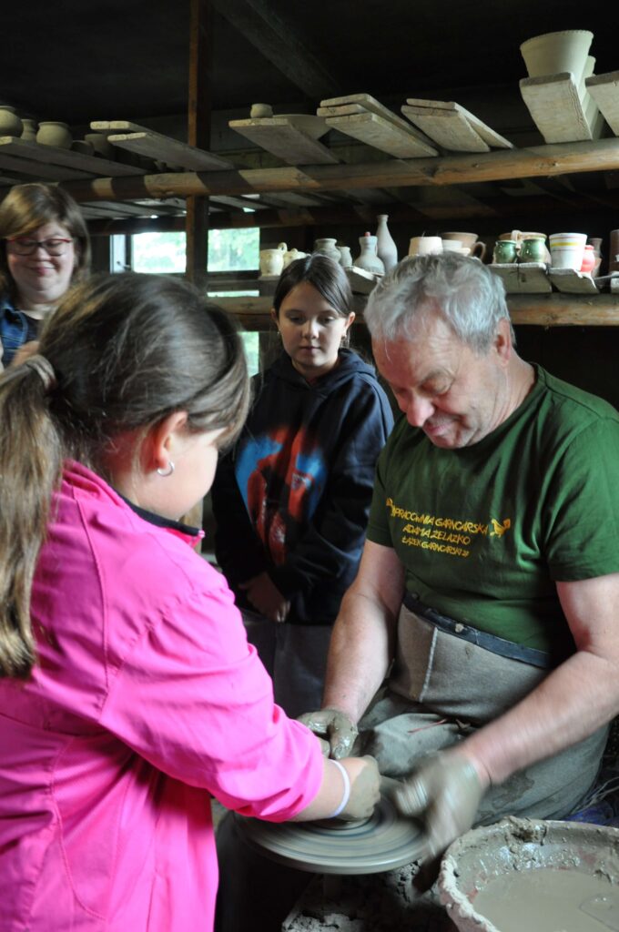 Dwoje dzieci i kobieta stoją wokół mężczyzny, który pracuje na kole garncarskim.