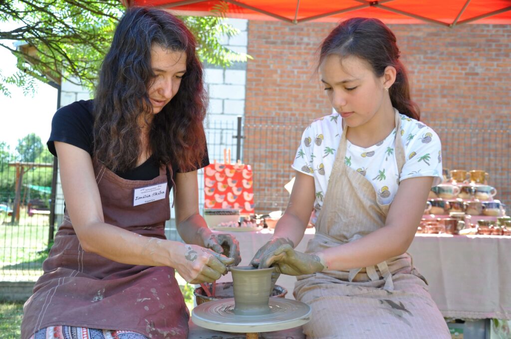 Kobieta wspólnie z dziewczynką tworzą ceramikę na kole garncarskim.