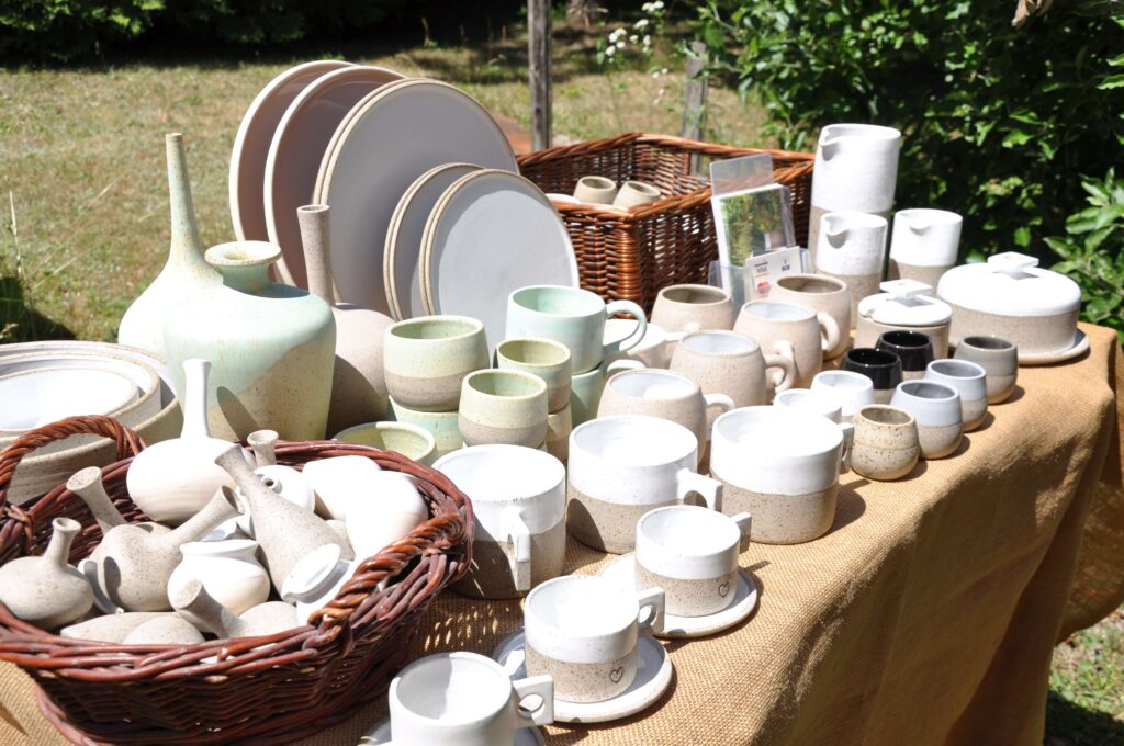 Stół z różnorodnymi wyrobami ceramicznymi, kubkami, flakonami, talerzami.