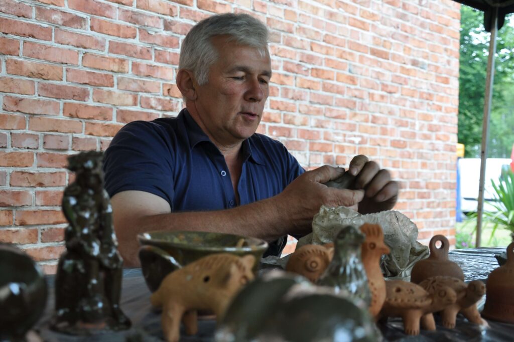 Mężczyzna tworzy ceramikę na stole, skupiony na formowaniu gliny.