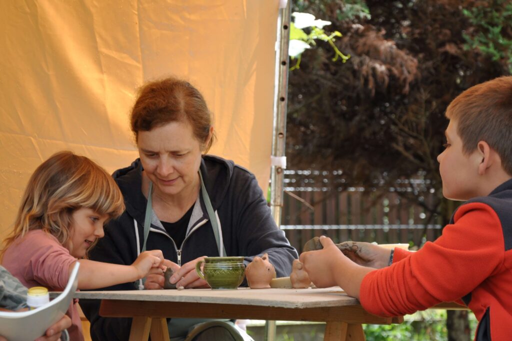 Dzieci przy stole z kobietą, wszyscy zaangażowani wspólne wykonywanie przedmiotów w glinie.