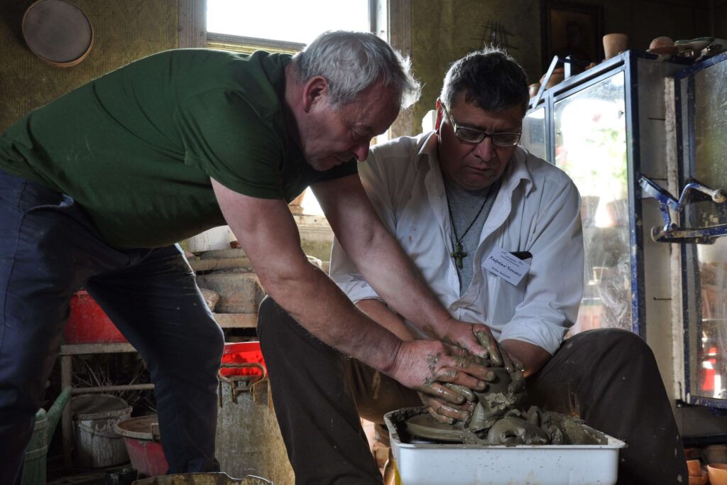 Dwóch mężczyzn podczas pracy nad ceramiką na kole garncarskim.