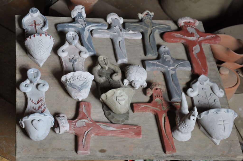 Stół pokryty wieloma wyrobami ceramicznymi - krzyżami, figurkami, kropielniczkami w różnych formach i kolorach.