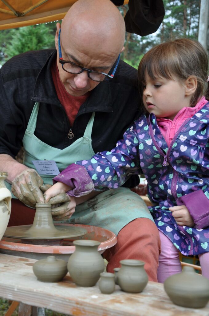 Mężczyzna i mała dziewczynka wspólnie lepią ceramikę siedząc przy kole garncarskim.