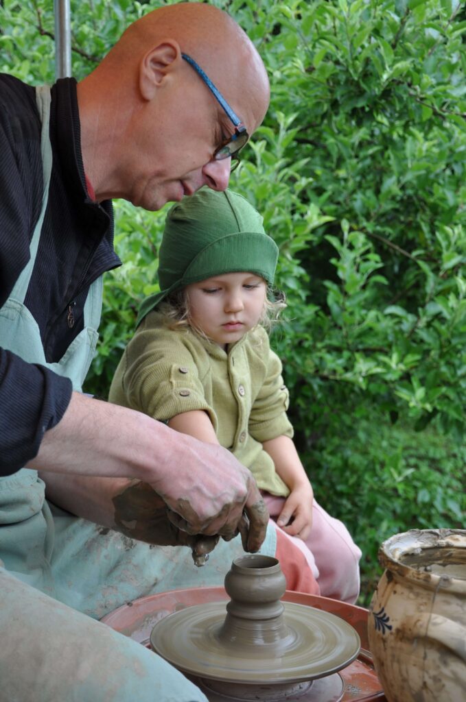 Mężczyzna i mała dziewczynka wspólnie lepią ceramikę siedząc przy kole garncarskim.
