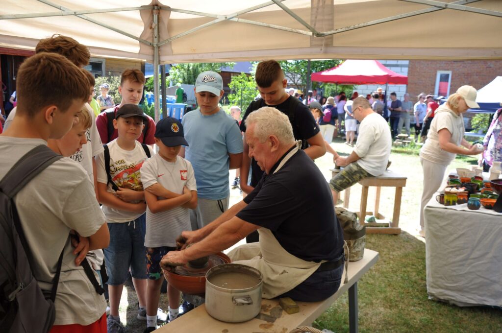 Ludzie stoją wokół garncarza podczas wydarzenia na świeżym powietrzu, obserwując jego pracę.