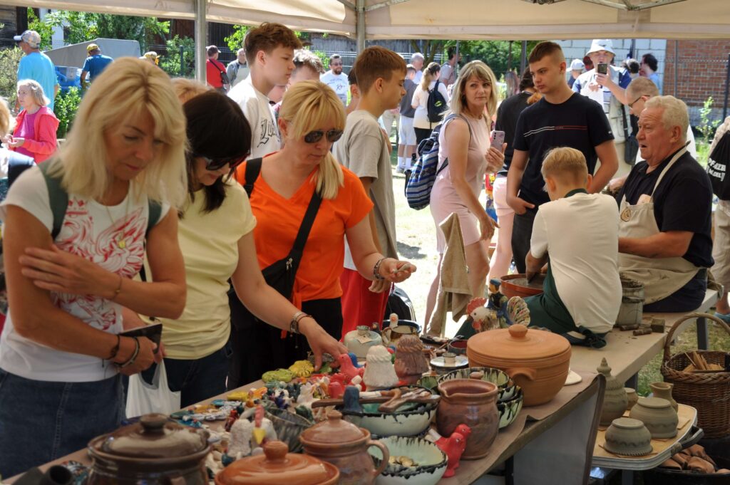 Ludzie oglądają ceramikę na stole, z zainteresowaniem przyglądając się różnorodnym przedmiotom.