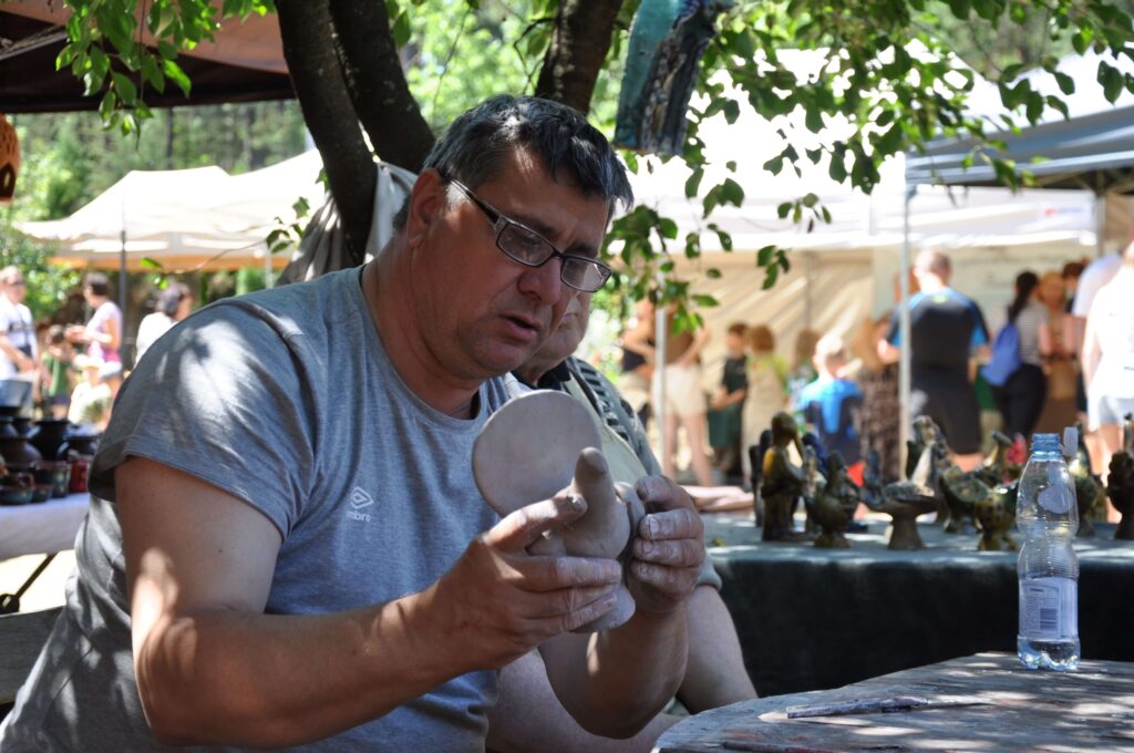 Mężczyzna formuje ptaka z gliny, skupiony na swojej pracy i technice.