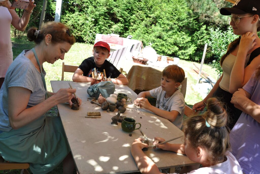 Kobieta z dziećmi siedzi przy stole, wszyscy skupieni na twórczej pracy z gliną.