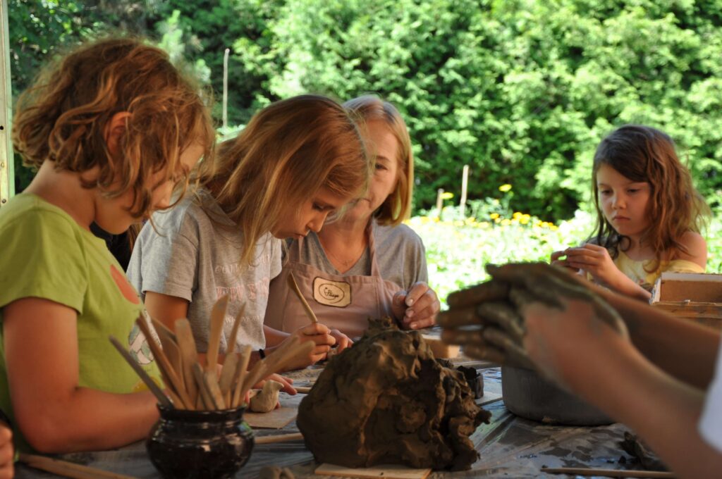 Kobieta z dziećmi siedzi przy stole, wszyscy skupieni na twórczej pracy z gliną.