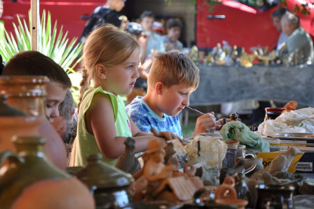 Dzieci siedzą przy stole, wszyscy skupieni na twórczej pracy z gliną.