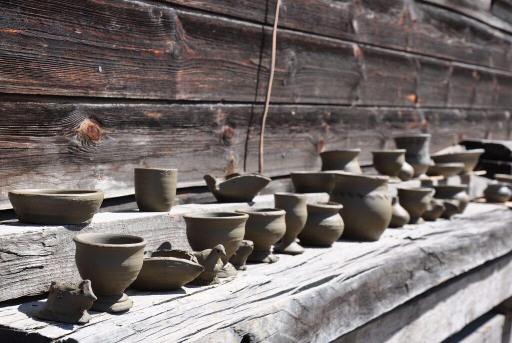 Naczynia gliniane schną w słońcu ułożone na belkach z drewna na tle ściany starego domu.