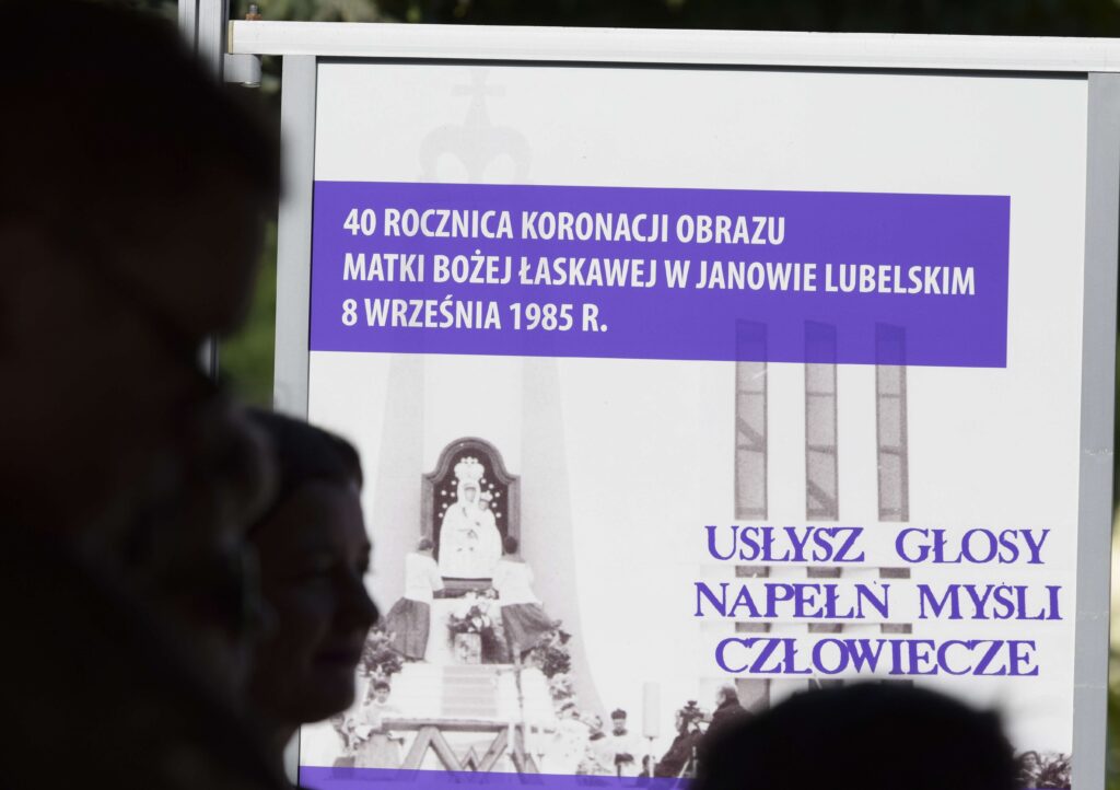 Zdjęcie czarno białe z napisami na niebieskim tle z uroczystości religijnych, na pierwszym planie niewyraźne postacie ludzi