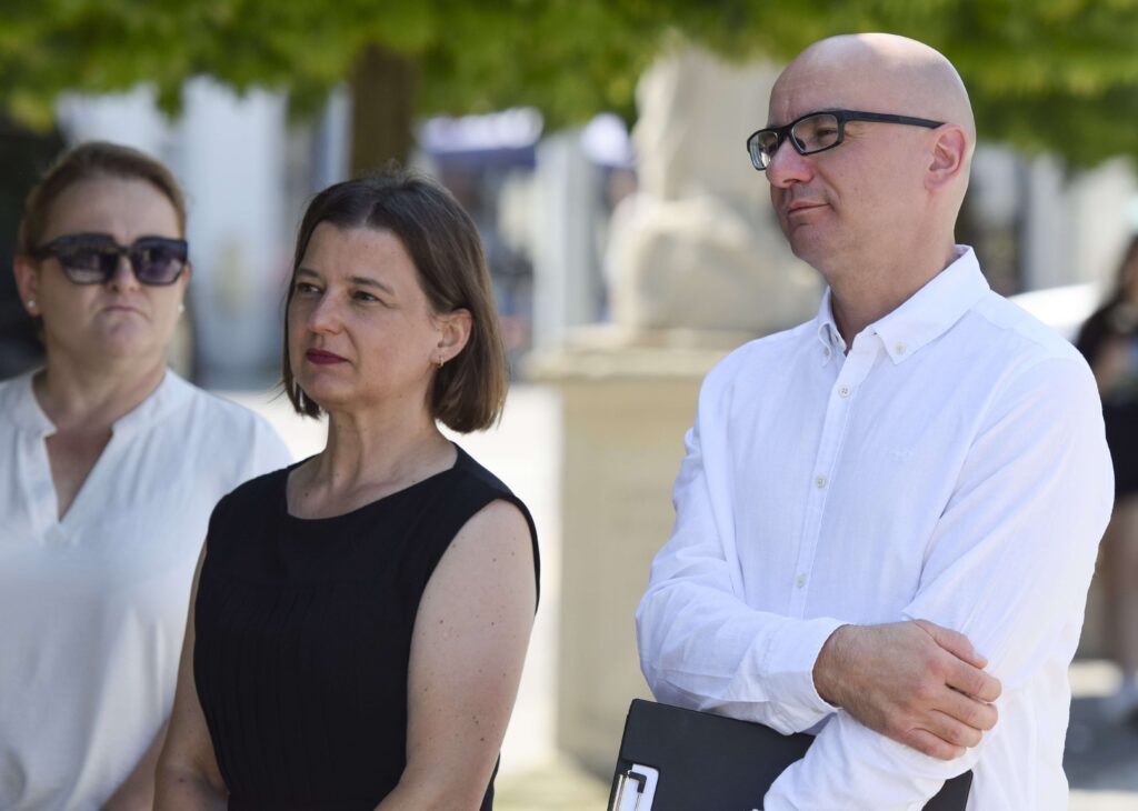 Kobieta w czarnej sukience i mężczyzna w białej koszuli stoją na tle drzewa.