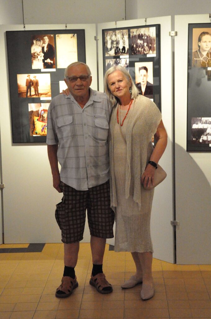 Kobieta i mężczyzna pozują do zdjęcia na tle ściany z zawieszonymi na niej zdjęciami.