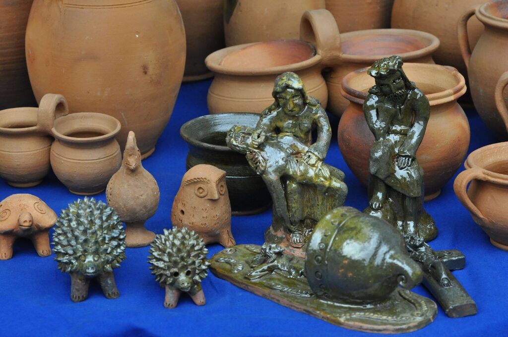 Ceramiczne naczynia i figurki w różnych odcieniach brązu i zieleni na niebieskim tle.