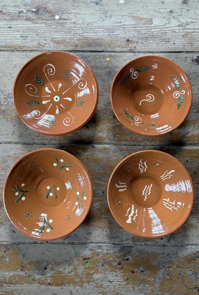 Cztery brązowe ceramiczne miski z białymi i zielonymi zdobieniami, ułożone na drewnianej, postarzałej powierzchni.
