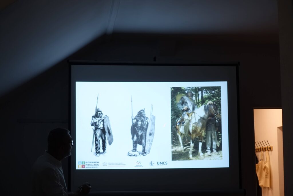 Człowiek na tle rzutnika z ilustracjami rycerzy w zbroi, tarczach i włóczniach oraz rycerza na koniu w lesie. Widoczne logo UMCS i inne symbole.